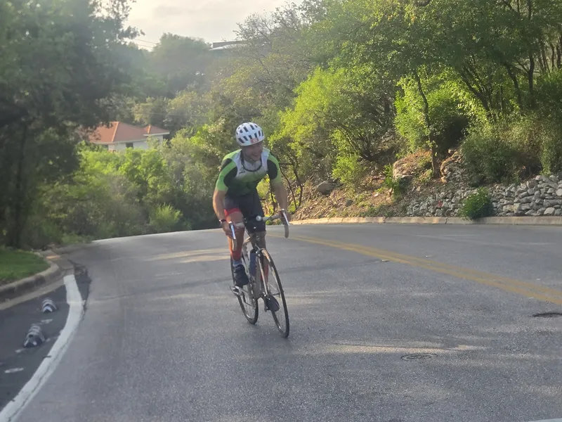 A rider in a green jersey climbing a curvy road outside Austin.
