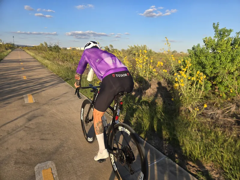 A rider in a purple kit on a bike path at sunset, wildflowers along the edge.