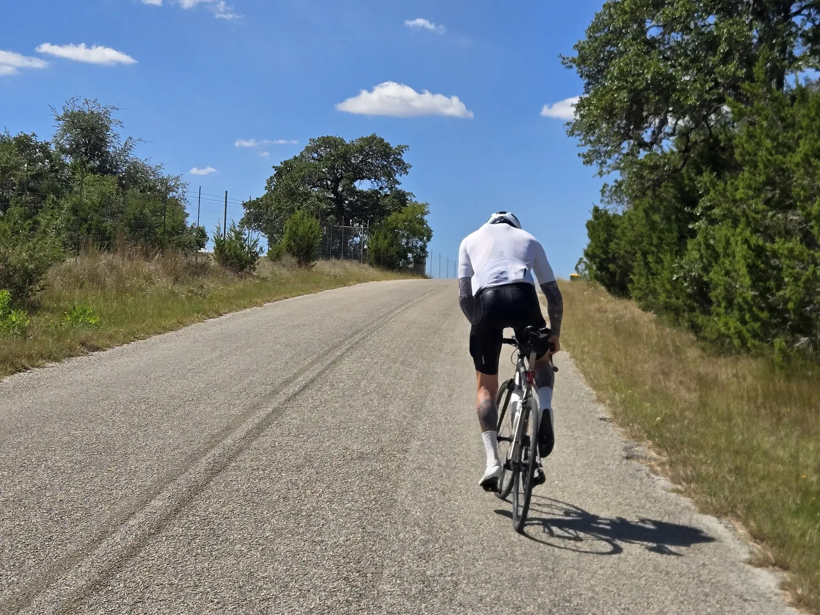 A rider in a white jersey climbing in the Hill Country.